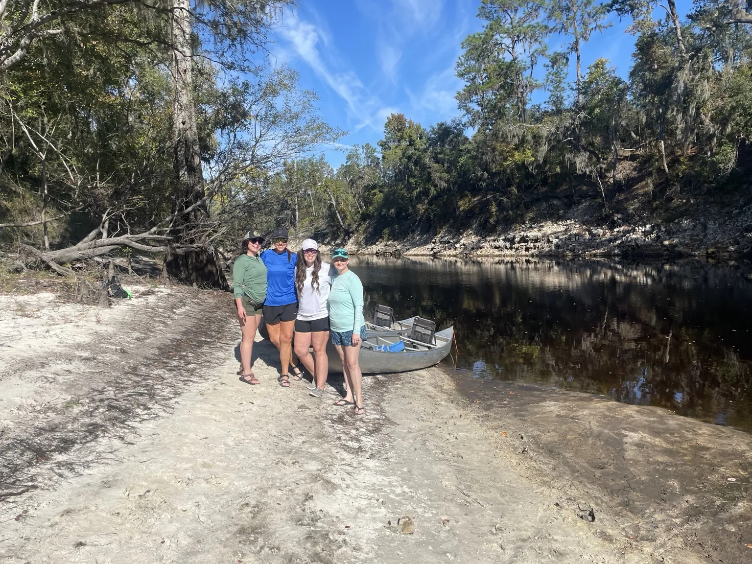 Group of paddlers standing beside canoes on a white sandbar along the Suwannee River