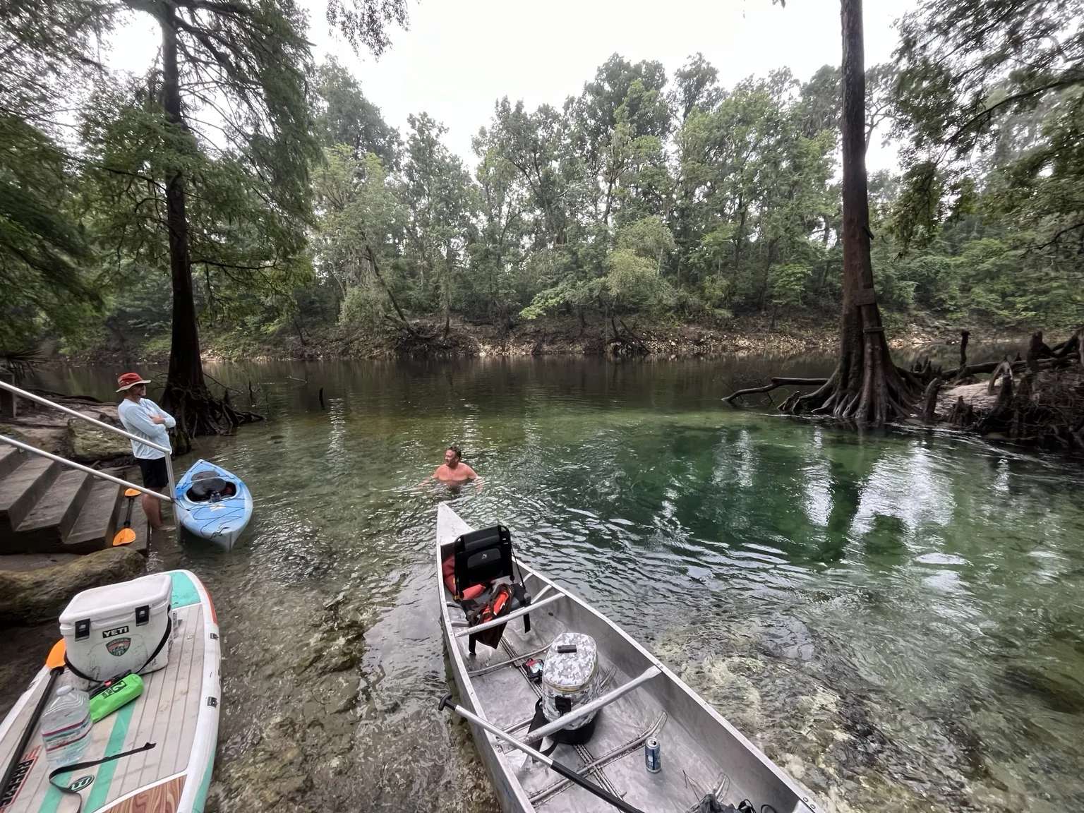 Clear spring water canoes paddleboards and swimmers at a quiet river spot surrounded by cypress trees